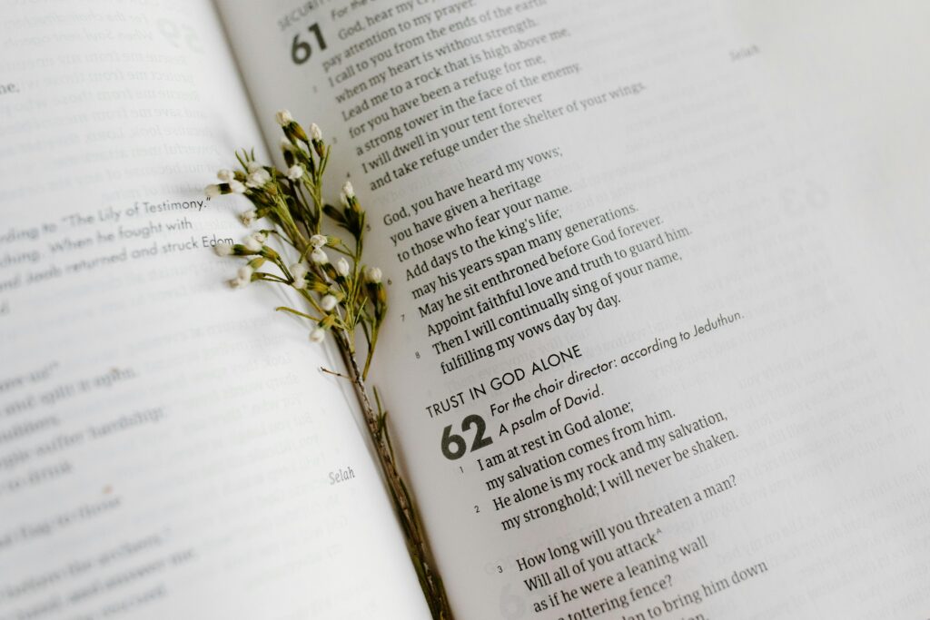 A close-up of an open Bible page with scripture and delicate white flowers.